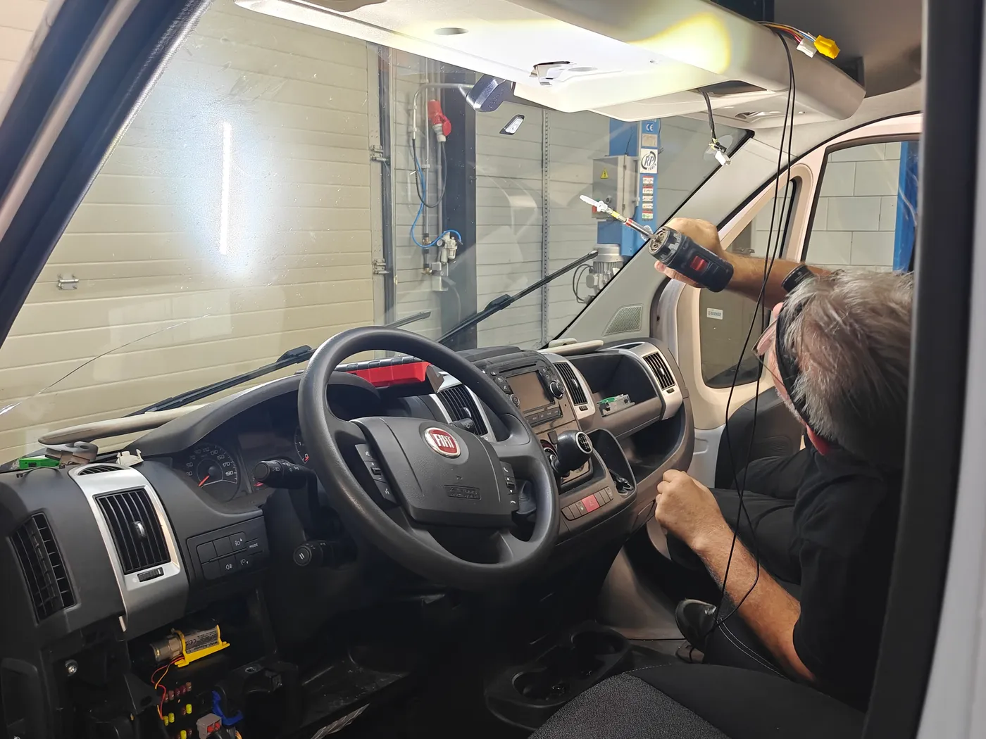 Monteur van Tacho Nederland trekt de tachograafbekabeling langs de A-stijl van een Fiat Ducato