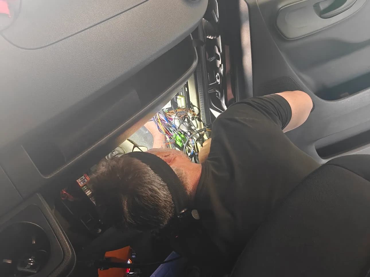 Monteur werkt aan de bekabeling onder het dashboard van een bestelwagen